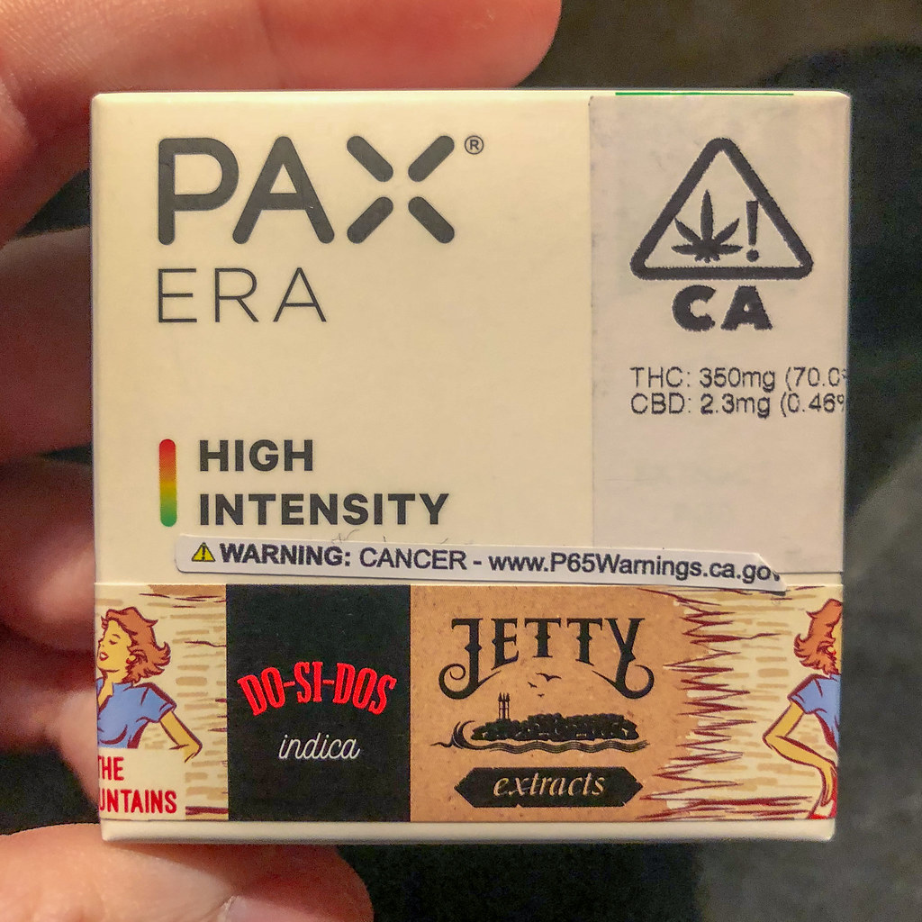 Hand holding a PAX Era high intensity pod box with California cannabis warning label
